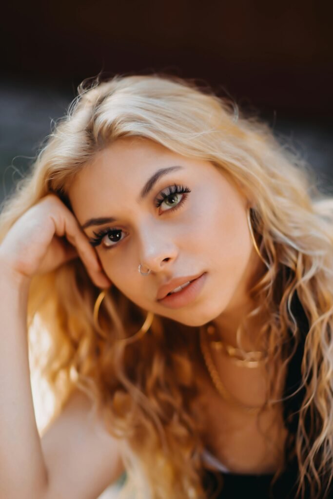 mulher loira cabelos ondulados loiros leve maquiagem b rincos argolas grandes pearcing no nariz uma das mãos segurando a cabeca Desi Perkins a influencer que está redefinindo beleza global