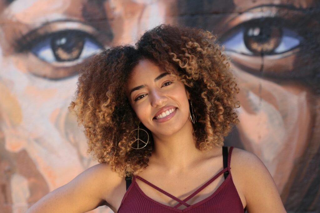 mulher linda leve maquiagem sorrindo cabelos crespos longos brincos argolas grandes blusinha com alca estilosa cor roxa