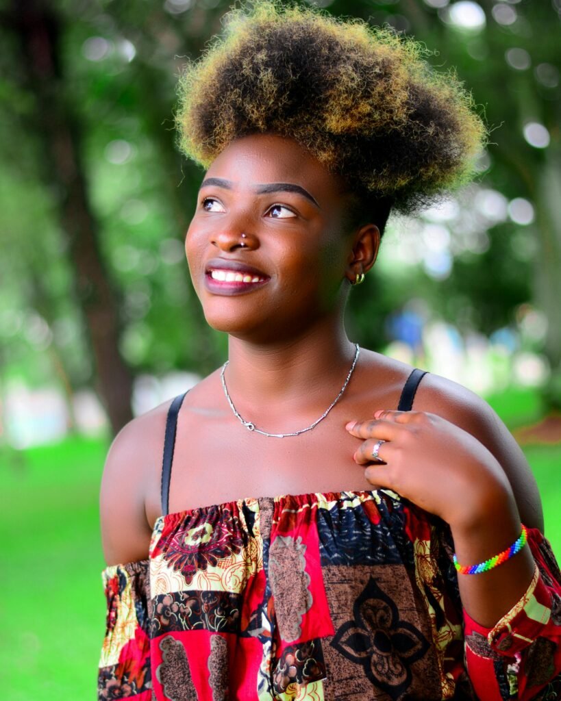 foto de mulher sorrindo cabelos crespos estilosos brincos argolas pequenos colar prata pearcing no nariz vestido colorido e pulseira colorida no braco