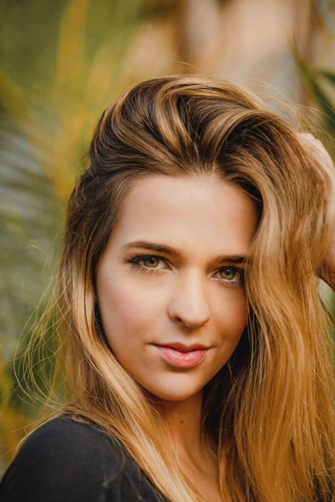 mulher loira olhos verdes claros leve maquiagem cabelos longos lisos uma das mãos nos cabelos