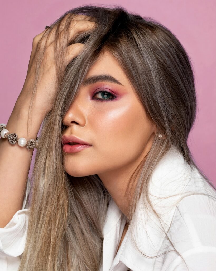 foto de mulher branca maquiada olhos azuis cabelos compridos lisos uma das mãos no rosto pulseira perola no braco