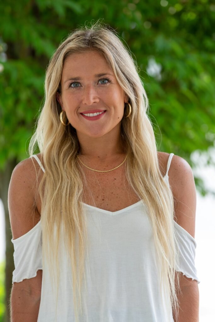 foto de perfil de mulher loira sorrindo cabelos longos lisos soltos brincos argolas médio olhos verdes blusinha branca social