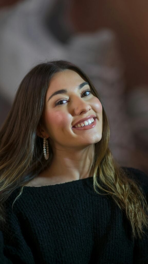 mulher sorrindo maquiada olhos castanhos cabelos longos lisos castanhos brinco argola com perolas blusinha preta