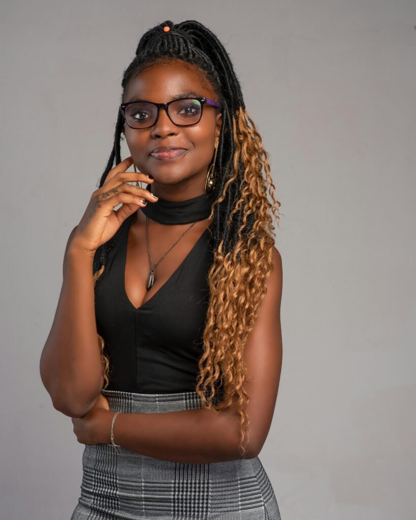foto de mulher preta jovem linda cabelo afro longo presto óculos leve sorriso e uma das mãos no rosto blusinha preta saia xadrez