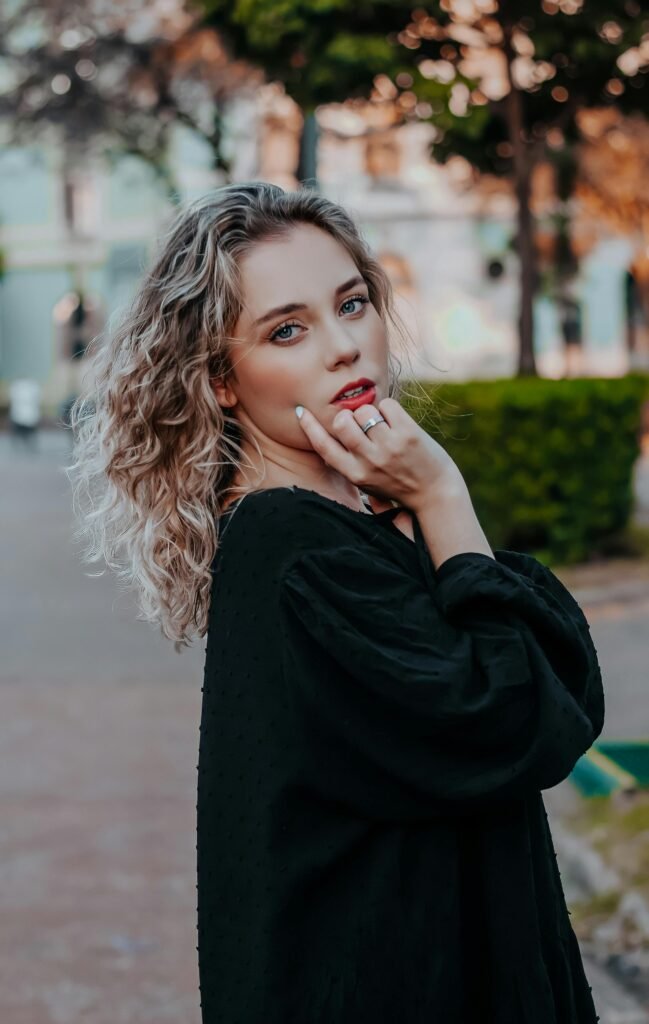 mulher loira olhos verdes maquiada loiros uma das mãos no queixo blusinha preta Layered shoulder length hair. Cabelo em camadas na altura dos ombros