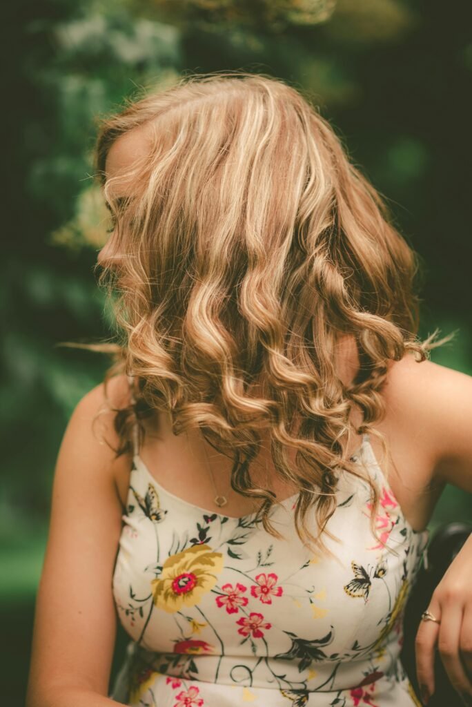 foto de mulher loira cabelos longos ondulados soltos na frente do rosto vestido com alca branca florido