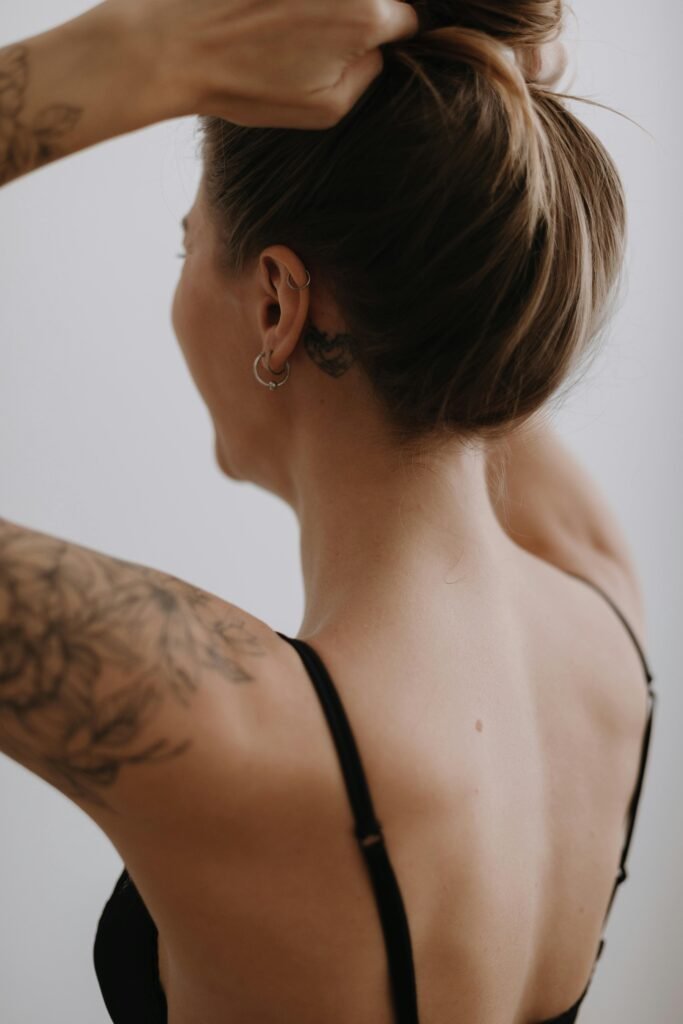 foto de mulher loira de costas cabelos presos french hair pin brincos e tatuagens sutiã preto