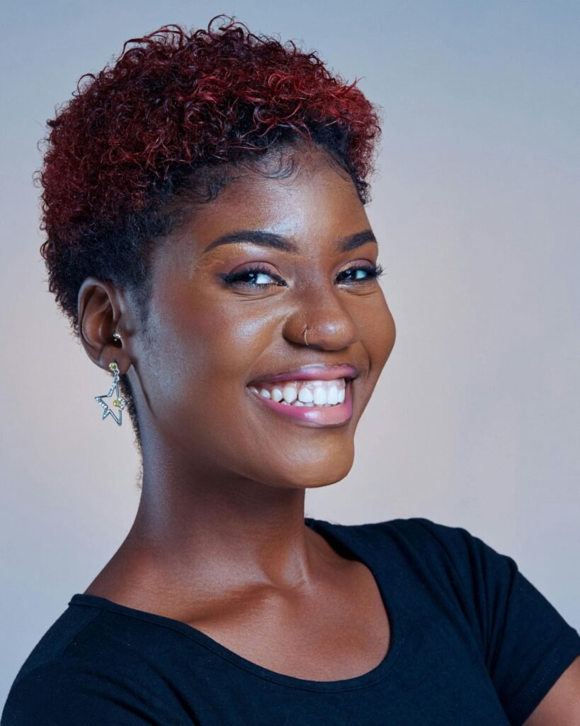 mulher sorrindo brinco estrela pearcing no nariz cabelos crespos curtos estiloso pintados de vermelho