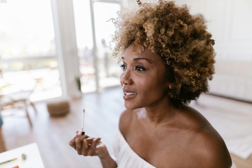 foto de mulher preta linda cabelo 3c encaracolados leve sorriso passando batom blusinha branca