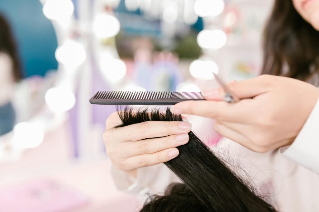 foto ilustrativa de corte de cabelo feminina cortando as pontas de cabelos lisos pretos mãos segurando tesoura e pente