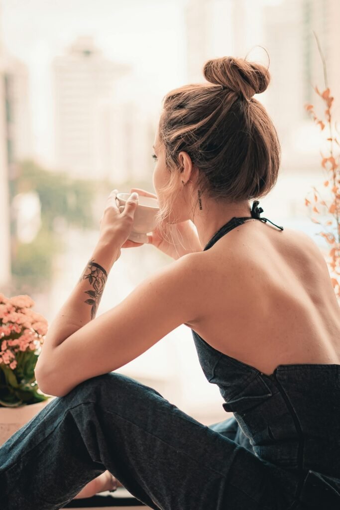 foto de mulher morena sentada tomando cafe em xícara cabelos presos coque french pin tatuagem no braco