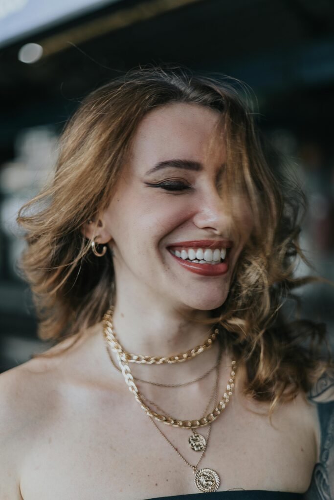 mulher branca loira sorrindo brinco pequeno na orelha colares de ouro Layered shoulder length hair. Cabelo em camadas na altura dos ombros