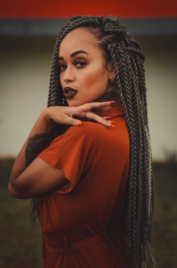 mulher preta linda maquiada brincos grandes redondos cabelos com varias trancas tatuagem no braco unhas laranja vestido estiloso marrom Vintage black lipstick