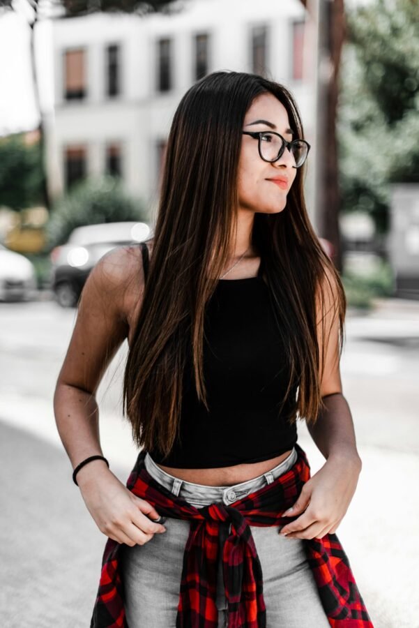 mulher sorrindo de óculos cabelos compridos lisos castanhos blusinha preta calca jeans blusa na cintura xadrez foto de Ras Jayamaha unsplash.com