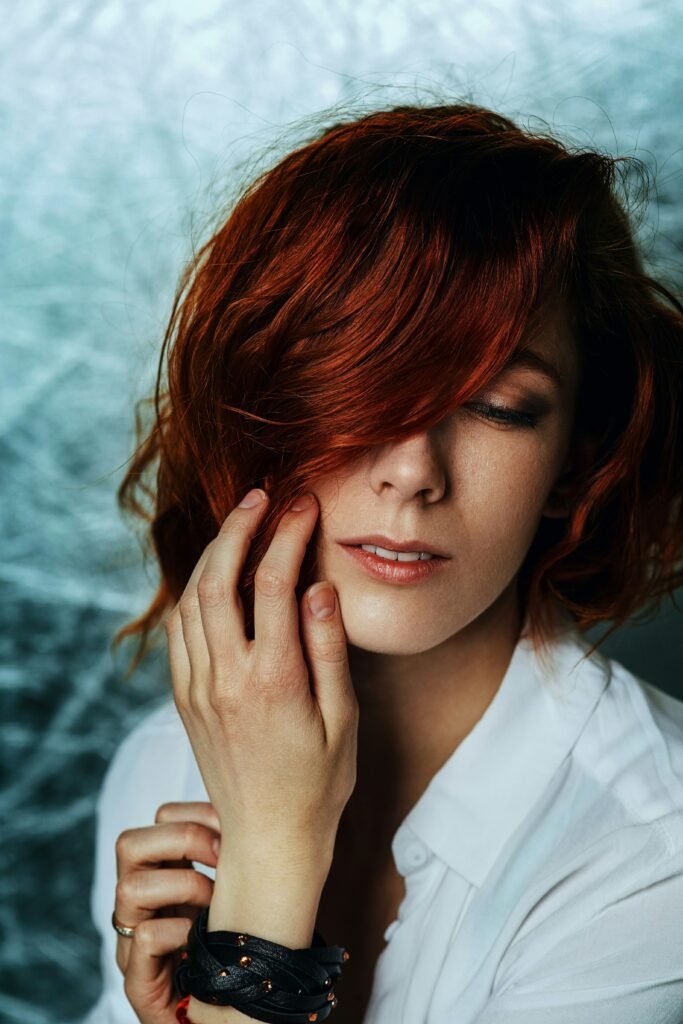 mulher corte de cabelo bob cut corte chanel cabelo cor vermelho blusinha branca uma das mãos no rosto