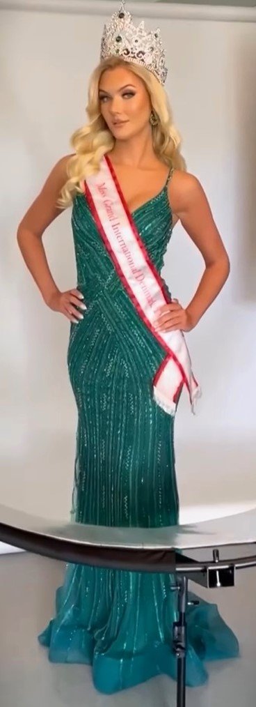 Victoria Kjaer Theilvig as Miss Grand Denmark  loira cabelos longos lisos vestido social estiloso de festa verde e coroa de mis Dinamarca esta com uma faixa de mis Dinamarca