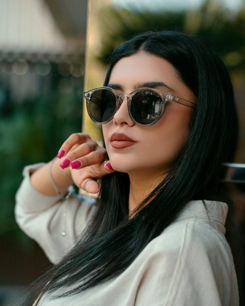 mulher maquiada óculos estiloso batom marrom cabelos lisos longos pretos unhas cor rosa blusinha branca