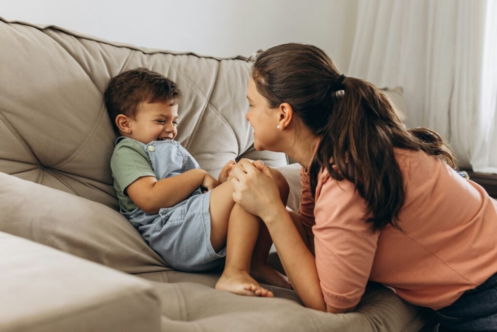 mãe brincando com seu filho pequeno no sofá da sala ambos sorrindo