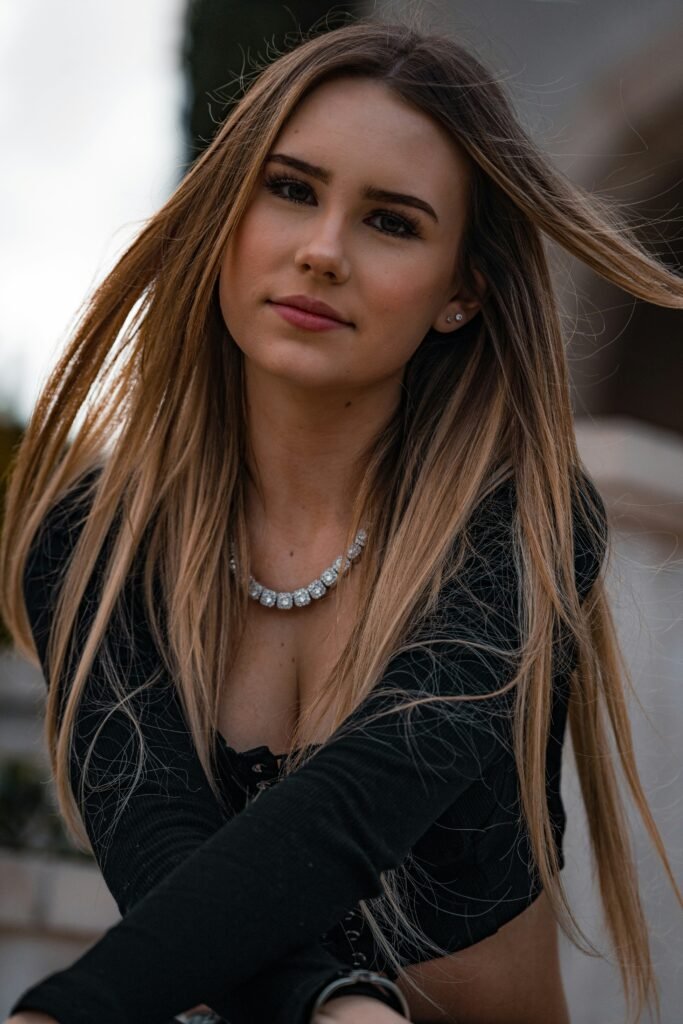 jovem mulher leve sorriso e maquiagem dois brincos pequenos de brilhantes cabelos lisos longos loiros blusinha preta bracos cruzados