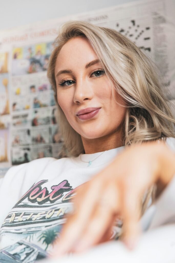 mulher loira olhos azuis leve sorriso cabelos lisos longos camiseta branca