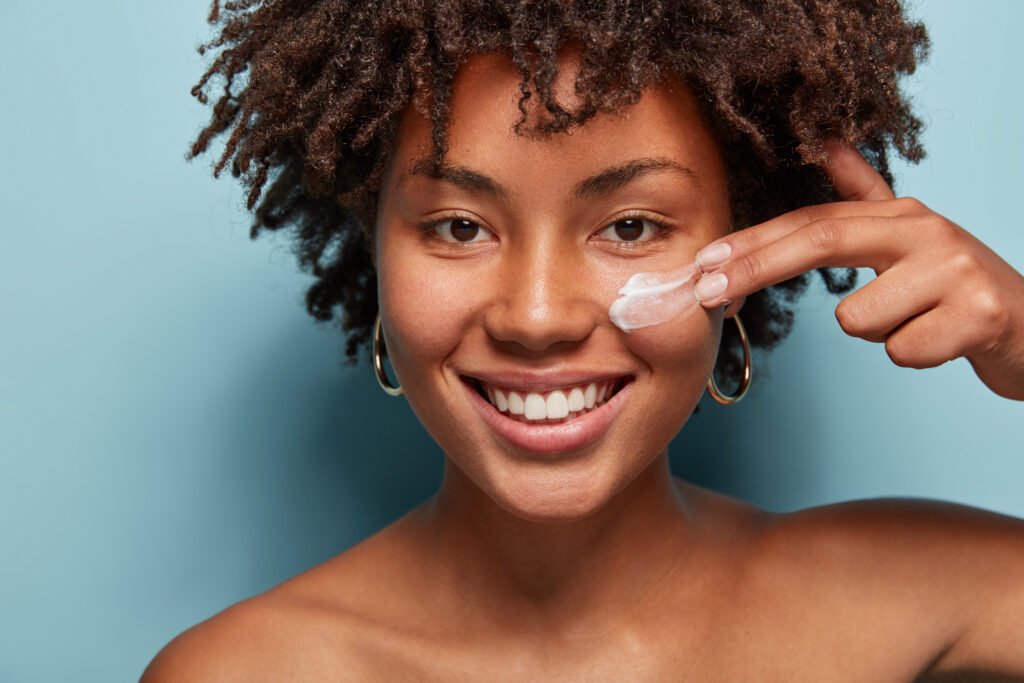mulher sorrindo olhos castanhos cabelos crespos médio estiloso brincos argolas médios dourados guia definitivo de sunscreen cream protetor solar tudo que você precisa saber