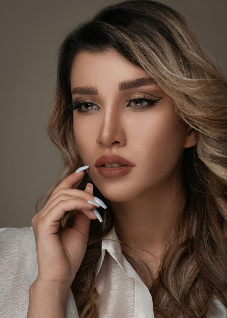 mulher maquiada batom marrom cabelos loiros lisos longos unhas brancas camisa social branca